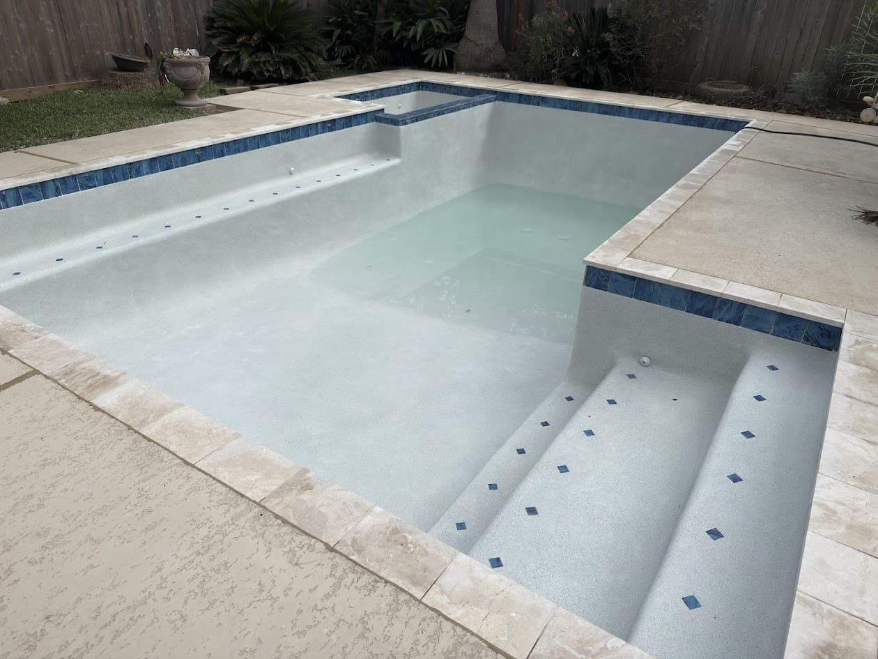 Same pool after renovation, fresh white plaster, blue tile, and travertine deck