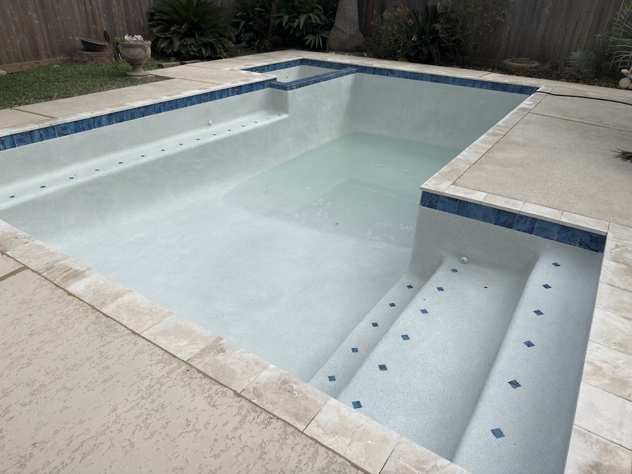 Same pool after renovation, fresh white plaster, blue tile, and travertine deck
